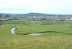 Blick auf das Dorf Aginskoje mit dem Fluss Aga im Vordergrund, der durch eine grüne Wiesenlandschaft mäandert