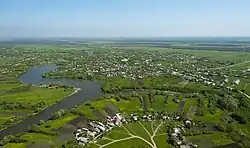 Luftbild von Kelermesskaja: Ein Fluss schlängelt sich durch eine grüne Landschaft mit einigen Häusern