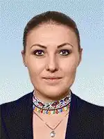 Sofija Fedyna mit neutralem Gesichtsausdruck. Sie trägt eine schwarze Jacke, die modern und schlicht wirkt. Sie hat mehrere Halsketten um den Hals. Eine davon ist silbern mit einem kleinen Stern-Anhänger, und eine andere ist bunt gestaltet mit verschiedenen kleinen Anhängern, die an eine kreative, individuelle Auswahl erinnern. Der Hintergrund des Bildes ist einheitlich und in einem hellblauen Farbton gehalten, wodurch die Person im Vordergrund besonders hervorsticht.