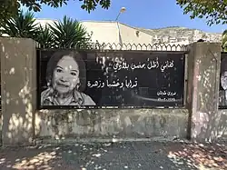 Zeichnung des Gesichts ab Schulter an einer Mauer von vorn rechtsseitig auf schwarzem Hintergrund mit linksseitigen arabischen Schriftzeichen.