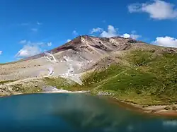 Im Vordergrund ist ein Ausschnitt des Sees am Fuße eines Berges zu sehen