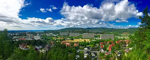 Foto einer von Wald umgebenen Siedlung. Im Vordergrund Wohnhäuser, dahinter große Wohnblöcke