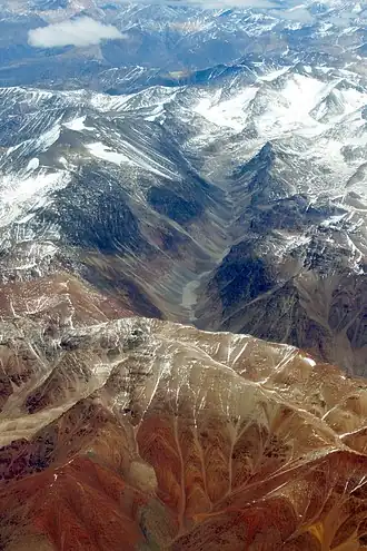 Im Vordergrund der Cerro Blanco mit seiner charakteristischen rötlichen Farbe die ihn von anderen Bergen unterscheidet. Dahinter die Quebrada de La Jaula zwischen dem Cordón del Plata (links), und dem Cordón de La Jaula (rechts). Blick von Norden aus ca. 10 km Höhe.