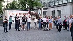 Jagdhornbläser Damme vor dem Mann mit Hirsch und einem Corona-Testzentrum, 2022