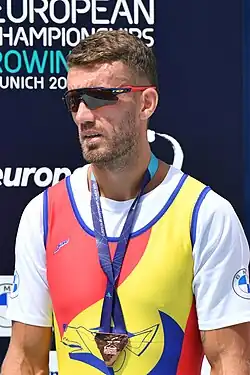 Enache trägt ein gelb-rotes Trikot, seine Medaille hängt an einem blauen Band um seinen Hals.