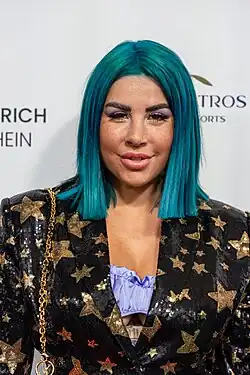 Porträt Kate Merlan in einem schwarzen Kleid mit goldenen Sternen und mit türkis gefärbtem Haar