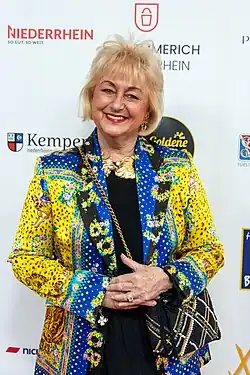 Stefanie Simon in einer blaugelben Jacke mit bunten Punkten vor Werbewand