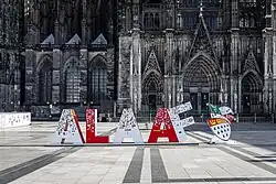 Vor der Fassade des Kölner Doms sind rote und weiße, ca. 1,50 m hohe Buchstaben aufgestellt, die das Wort „Alaaf“ bilden.