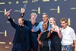 Gruppenaufnahmen "Die Discounter" mit Fernsehpreis auf rotem Teppich vor grauer Wand mit Senderlogos