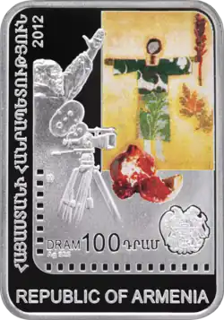 Eine hochkant stehende rechteckige Münze. Darauf sind eine Kamera, ein Bild mit einem grün gekleideten Mann, ein aufgeschnittener Granatapfel und ein Wappen abgebildet. Dazu der „Republic of Armenia“ und „DRAM 100“