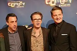 Alexander Schubert, Matthias Matschke und Holger Stockhaus posieren gemeinsam beim Deutschen Comedypreis 2017 vor einer Wand mit dem Schriftzug 'Deutscher Comedypreis'. Alexander Schubert trägt ein schwarzes Hemd und einen schwarzen Anzug. Matthias Matschke ist in einem gemusterten Hemd und einem dunklen Blazer gekleidet. Holger Stockhaus trägt ebenfalls ein schwarzes Hemd und einen schwarzen Anzug, ergänzt durch ein weißes Einstecktuch. Die drei Männer stehen nebeneinander und blicken in die Kamera.