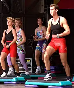 Vier Personen trainieren mit Hanteln in den Händen und stehen hinter Trittgeräten aus Kunststoff.