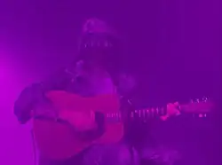 Angela Aux im Bühnenkostüm mit Kapuze und Gesichtsschleier, umwabert von lila Kunstnebel