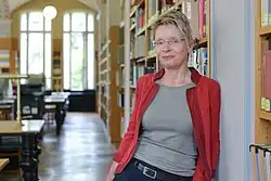 Anke Berghaus-Sprengel steht an ein Regal gelehnt in einem Lesesaal.