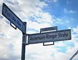 Foto eines weißen Straßenschildes mit schwarzer Schrift "Annemarie-Renger-Straße", das an einem Metallpfahl befestigt ist
