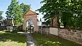 Zugangstor zum Friedhof mit zwei Stationen des Kreuzweges