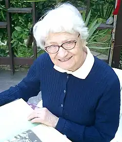 Asuman Baytop. Eine ältere Frau in Strickjacke im Stuhl mit einem Pflanzenbuch auf dem Schoß. 2003