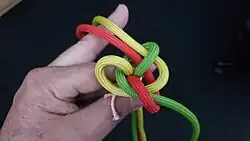 Mit dem gelben Kardeel wird gleich verfahren. Es wird unter das grüne Auge durchgesteckt und liegt parallel zum roten Kardeel.