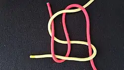 Dann fährt man in der Draufsicht von rechts unten kommend mit dem anderen Ende (hier rot) unter, über und nochmal über das hier zur Vereinfachung gezeigte gelbe Ende, wendet und unter, über und unter wieder zurück, wendet wieder und über, nochmal über und unter wieder nach oben.