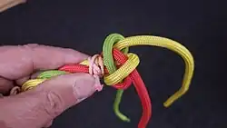 Nun nimmt man den Knoten seitlich und zieht ihn an den Enden leicht zu, aber noch nicht ganz.