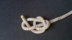 Nun führt man die lose Part über die stehende Part nach unten und führt sie durch die Bucht nach oben.