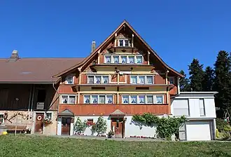 Der katholische Fridolin Anton Grob liess 1781 die gestrickte Fassade seines Hauses vertäfern und mit Klebdächern und einer Sonnenuhr versehen. Spilhusen, Mosnang[50]