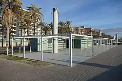 Foto einer Strandpromenade mit Palmen und Hotels, im Vordergrund zwei niedrige graugrüne Gebäude mit der Aufschrift Beach Club Six.