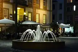 Beleuchteter Brunnen, im Hintergrund das Theater „TAM“.