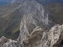 Blick vom Gipfel auf den Westgrat. Der Pfeil weist den Weg zum Abstieg auf das Zudrellband. Im Hintergrund die Südwände der Kirchlispitzen.