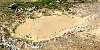 Satellitenaufnahme des Tarimbeckens mit der Taklamakan-Wüste; im Südwesten Ausläufer des Himalaya. Das Tian-Shan-Gebirge befindet sich im oberen Bildteil nördlich des Tarimbeckens. In der linken oberen Bildecke der Yssyk-Köl-See. (NASA/MODIS/Blue Marble)