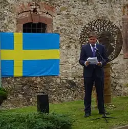 Bronzefarbene Metallskulptur auf einem ockerfarbenen Sandsteinsockel.