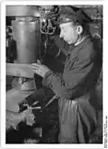Berliner Qualitätsbrigaden – VEB Hüttenwerk – Zu den Berliner Betrieben, die Qualitätsbrigaden gebildet haben, gehört auch das VEB Hüttenwerk Emil Schmidt in Berlin-Lichtenberg, Herzbergstraße 35. Hier wird aus Flugzeugschrott hochwertiges Material für unseren Wirtschaftsaufbau gewonnen. Im Betrieb ist eine 18 Mann starke Aktivisten- und Qualitätsbrigade. Auf dem Bild der Aktivist Franz Stamm, der eine Vorrichtung ersann, durch die Sägeblätter im eigenen Werk geschärft werden können. Bisher hatten auswärtige Unternehmen diese Arbeit übernommen und dem Hüttenwerk so beträchtliche Unkosten verursacht. Datierung: 7. Dezember 1949, Fotograf: Gustav Köhler. Quelle: Bundesarchiv
