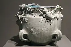 Übertopf aus hell lasierter Keramik mit einem Hochreliefdekor aus Putten und vier Henkeln an der Basis