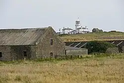 Ein Leuchtturm auf einem Hügel, im Vordergrund alte Steingemäuer.