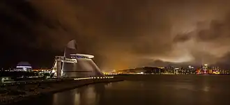 Eine Aufnahme bei Nacht zeigt das Science Center vor einem beleuchteten Horizont. Im Vordergrund ist ein Fluss zu sehen.