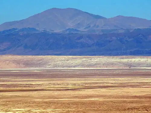 Die Cordillera Domeyko von den Hängen der Anden-Westkordillere aus gesehen. Auf 2.900 m ü. M. Höhe in 50 bis 70 km Entfernung in Richtung Westen betrachtet, erhebt sich hinter der Salar-de-Atacama-Senke (2.300 m ü. M.) und der Cordillera de la Sal der dunkle Steifen des El Bordo-Kliffs auf um die 3.000 m ü. M., vor dem höchsten Berg dem Cerro Quimal.