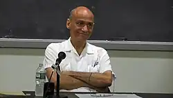 Charles Mills sitzt mit verschränkten Armen hinter einem Tisch.