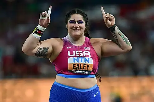 Die bewusst stark geschminkte Kugelstoßweltmeisterin Chase Ealey hebt ihre Hände mit hochgestreckten Zeigefingern nach oben.