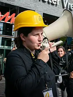 Witalina Kowal ist von Menschen umgeben und trägt einen gelben Helm. Sie spricht in ein Megafon, das sie in der Hand hält.