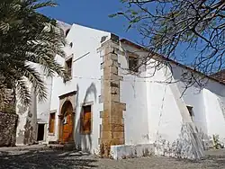 Außenansicht der Kirche unter Palmen mit vorspringenden Stützmauern.