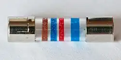 Feinsicherung 5×20 mm mit Farbkodierung ähnlich der von Widerständen. Der breite Streifen ist rechts, damit wird die Leserichtung festgelegt. Die Farbringe bedeuten: braun: 1 blau: 6 rot: 102 = 100 blau: Auslösecharakteristik und steht für 1600 mA, mittelträge