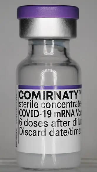Ungeöffnete und mit einem violetten Deckel versiegelte Phiole mit dem aufgetauten und noch unverdünnten mRNA-basierten COVID-19-Impfstoff des Handelsnamens Comirnaty. Die Höhe beträgt 40 Millimeter und der Außendurchmesser 16 Millimeter.