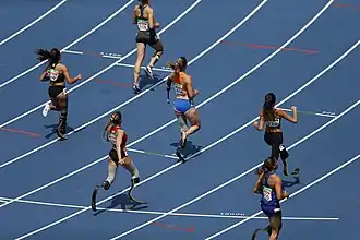 Die blauen Bahnen des Stadions erstrecken sich gleichmäßig, während die Läuferinnen in verschiedenen Formationen auf der Strecke unterwegs sind.