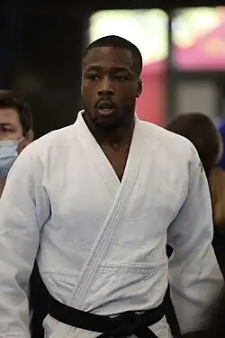 Diesse im weißen Kampfanzug, im Hintergrund trägt jemand eine Corona-Schutzmaske.