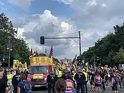 Demonstrationszug mit Lautsprecherwagen (links), Teilnehmenden (rechts), Fahnen und Transparenten.
