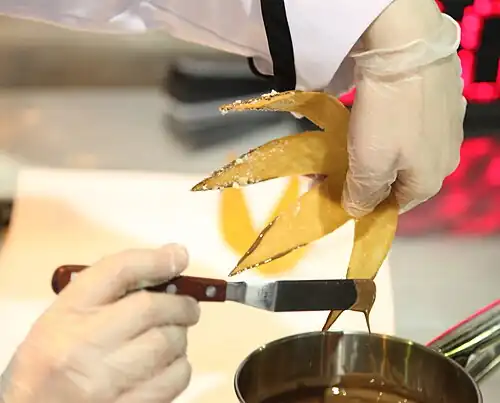 Verzieren einer Dessert­garnitur aus Gebäck mit „Knusperkanten“, mit Hilfe einer Palette