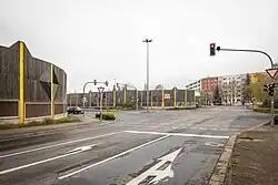 Foto einer großen Straßenkreuzung mit Ampel, Halteschildern und Richtungspfeilen auf zwei Fahrbahnen. Die Fahrbahnen sind teilweise mit Lärmschutzwänden begrenzt.