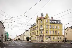 Foto einer Kreuzung mit Trambahnschienen und Oberleitungen aus bzw. in alle Fahrtrichtungen. Im Hintergrund ein ockerfarbenes Haus.
