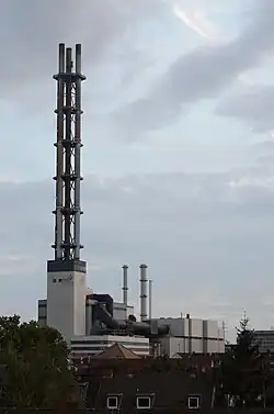 Stadtwerketurm mit den Unterbauten des HKW II sowie den Ersatzschornstein für HKW I und Heizwerk im Hintergrund (links, 2014); Nachtaufnahme mit der charakteristisch grünen Beleuchtung (2012)