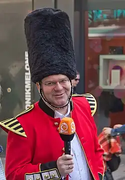 Abgebildet ist der Moderator Elton, gekleidet in eine an französische Uniformen des späten 19. Jahrhunderts erinnernde Karnevalsuniform des Kölner Karnevals mit einem hohen Fellhut